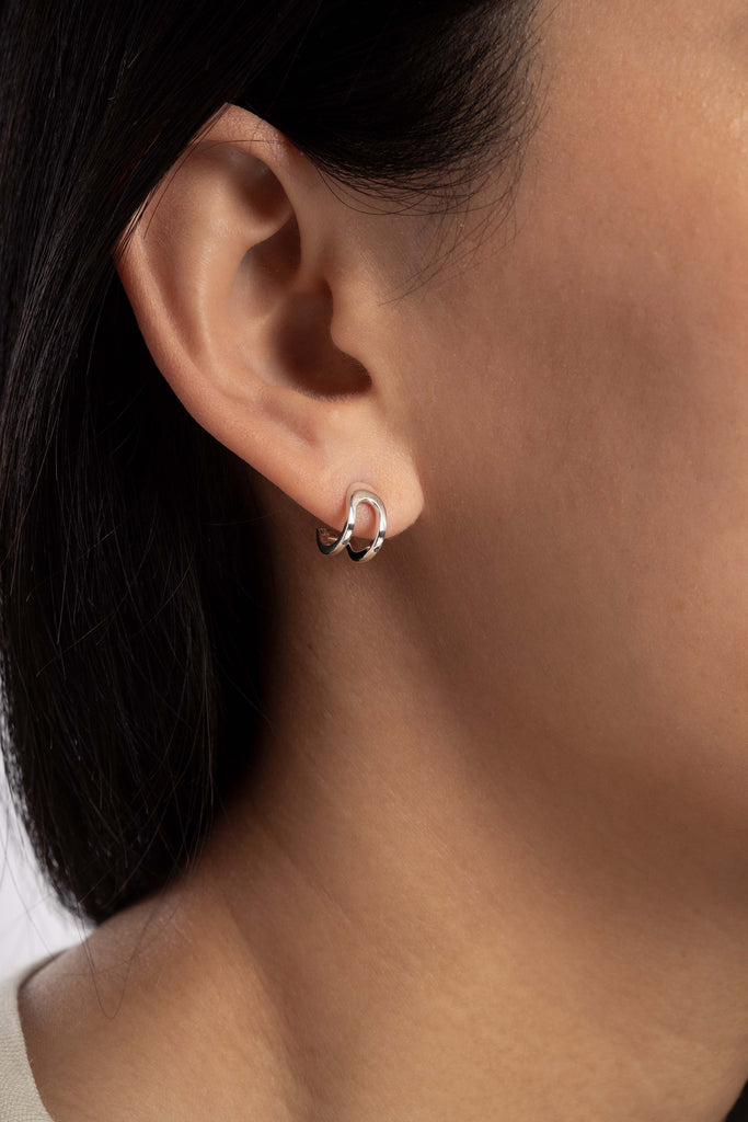 Boucles d'oreilles Maison Mouche au design épuré et architectural, en argent 100% recyclé et tracé, fabriquées dans des ateliers eco-responsables en Italie. Cette mini boucle L'AVENTURE enrobe discrètement l'oreille, elle est un jeu d’oppositions et de ruptures entre courbes et segments. Les biais accentuent les perspectives, la lumière avive les angles et découpe les espaces.