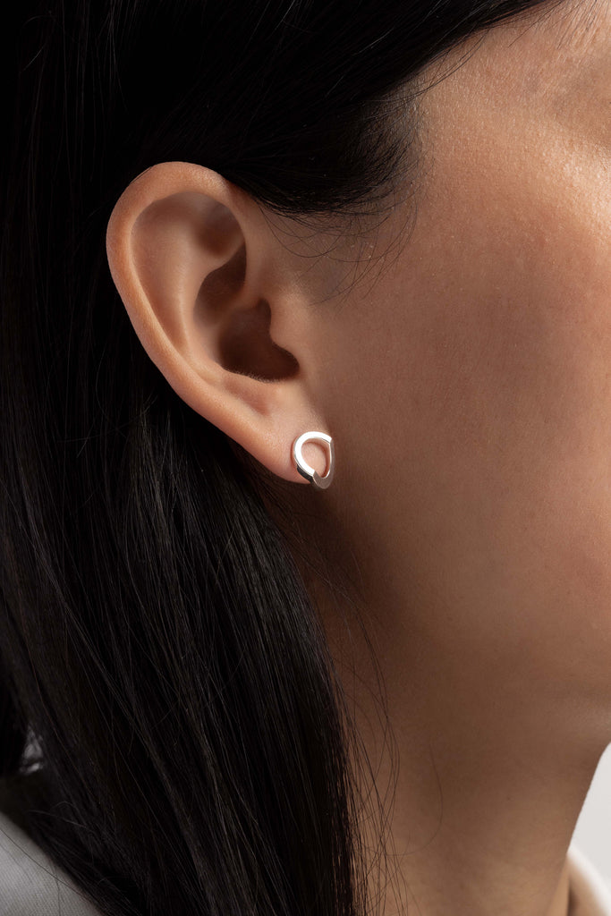 Boucles d'oreille Maison Mouche, cercle ou coeur ? Ces boucles soulignent le dessin de l'oreille et offrent une lecture surprenante de leur forme. Design épuré et minimaliste, en argent 100% recyclé et tracé, fabriquées dans des ateliers eco-responsables en Italie. La collection LE SECRET s’inspire des fascinants procédés optiques de l’anamorphose. Selon l'angle de vue, vous y verrez tantôt un cercle parfait, tantôt un croissant, tantôt un coeur dissimulé.